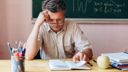 Middle age teacher in glasses attentively and tiredly reading textbook