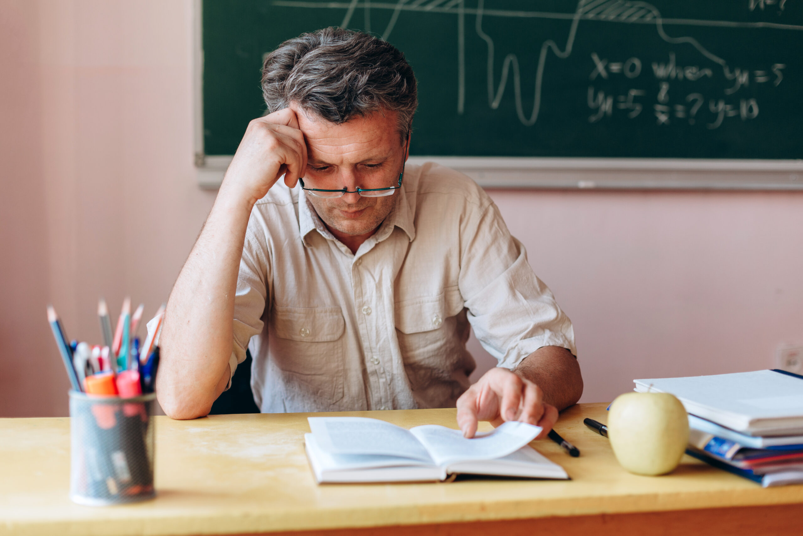 Middle age teacher in glasses attentively and tiredly reading textbook