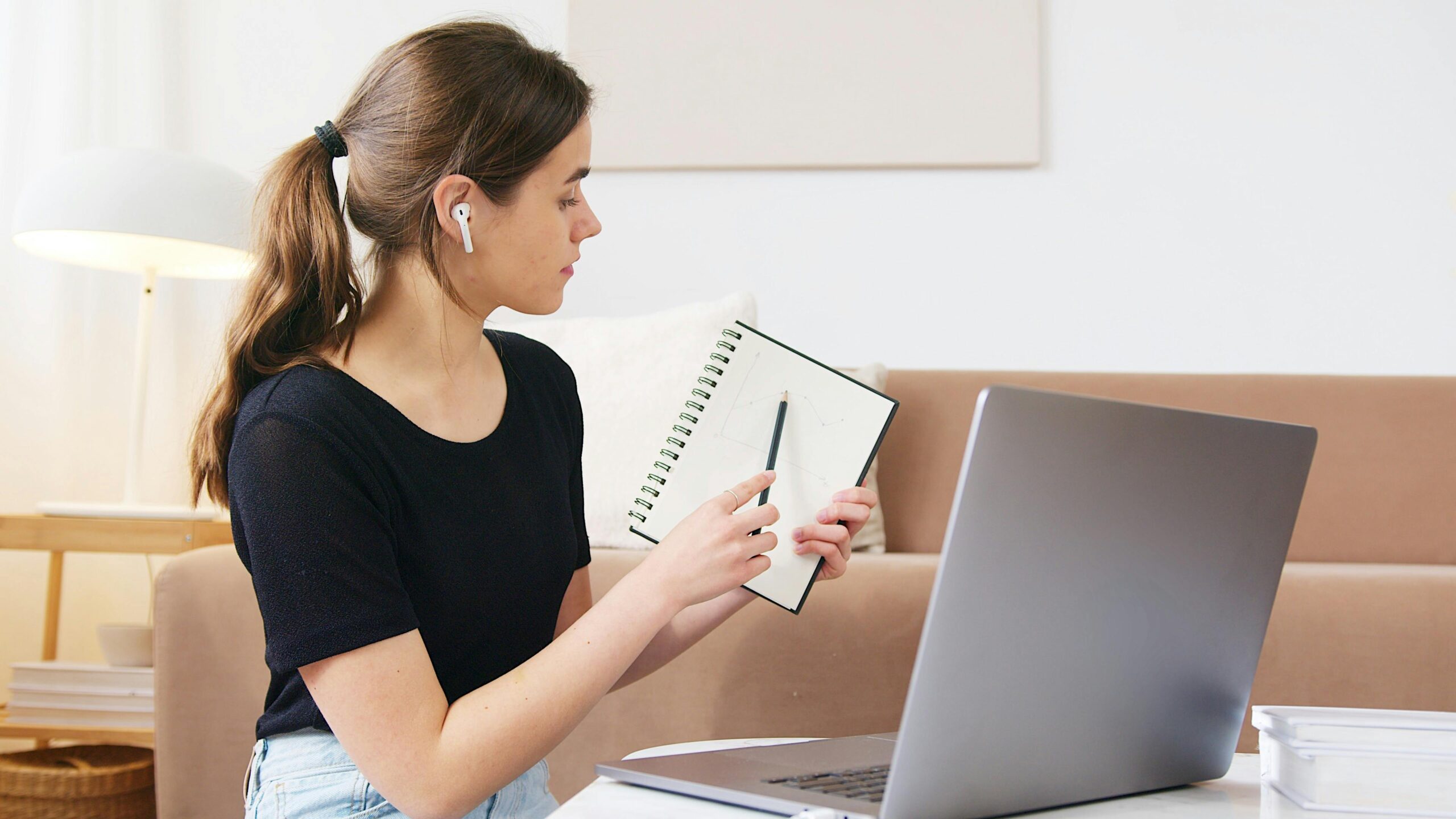 Person writing in notebook looking at laptop