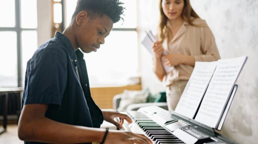 Young person playing piano while a teacher observes.