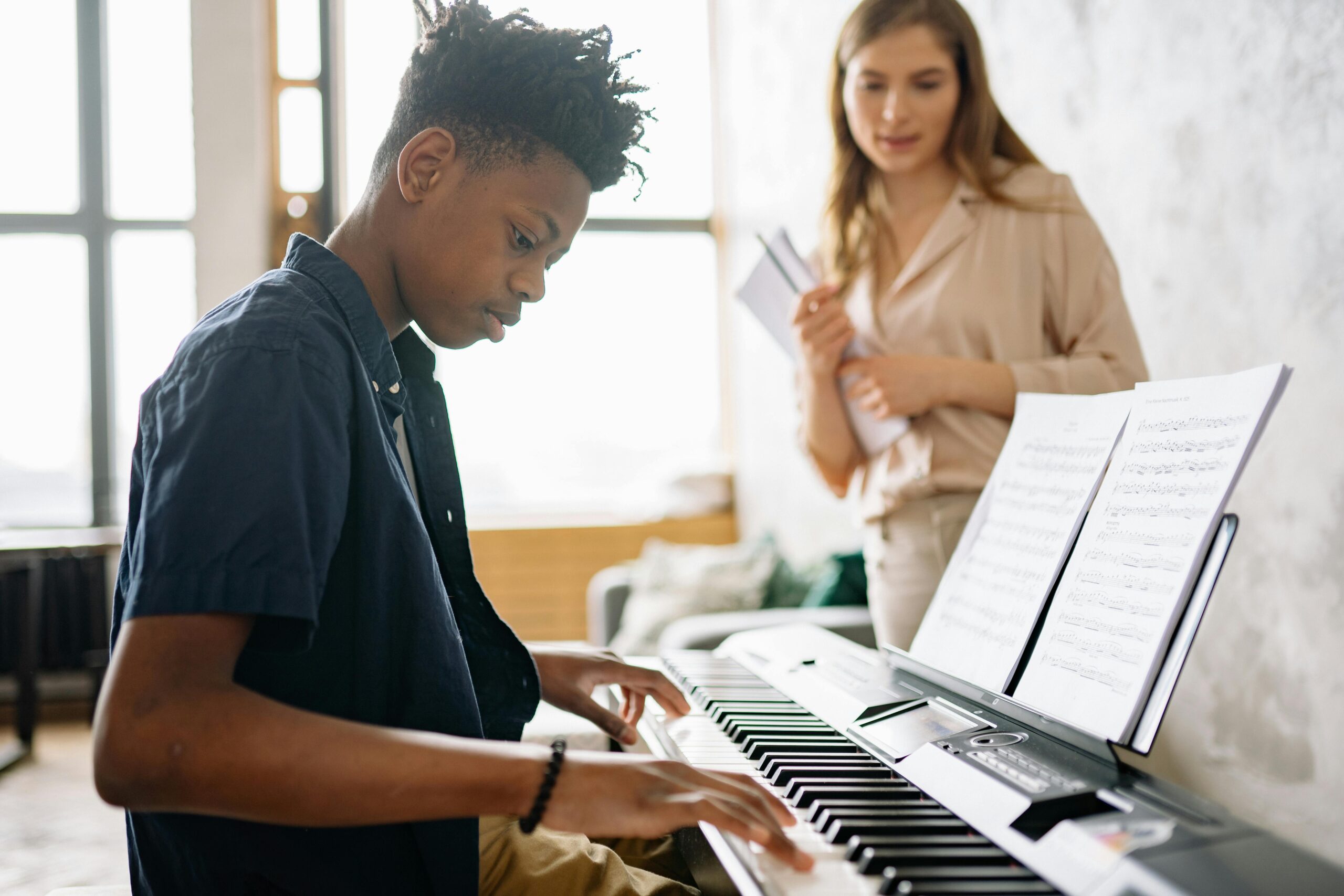 Young person playing piano while a teacher observes.